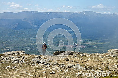 Hiker observing a village from a mountain top with a mountainous landscape in the background Stock Photo