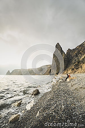 Hiker with an orange backpack enjoying sea view. Rocky seashore Stock Photo