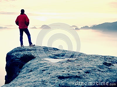 Hiker in red jacket enjoy view over clouds. Mountain rocky peak Stock Photo