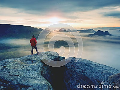 Hiker in red jacket enjoy view over clouds. Mountain rocky peak Stock Photo