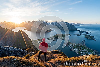 Hiker in red jacket are standing on top of the famous Reinebringen overlooking Reine and Hamnoy in the Lofoten islands during the Stock Photo