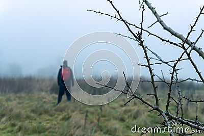 A hiker with red ruck sack standing in the distance in a out of focus. On a foggy, winters day in the countryside Stock Photo