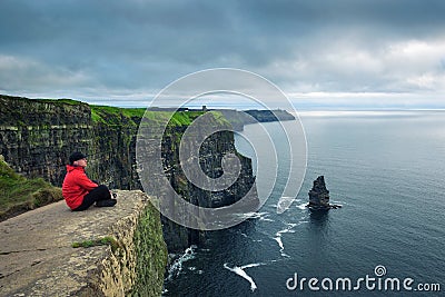 Hiker sitting at the cliffs of Moher Stock Photo