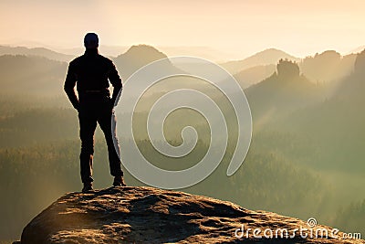 Hiker is standing on the peak of sandstone rock in rock empires park and watching over the misty and foggy morning valley to Sun. Stock Photo