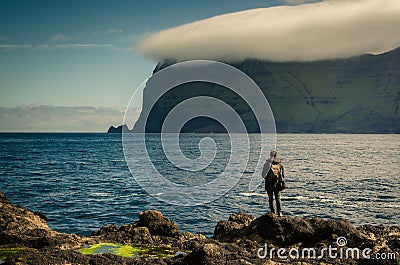 Hiker standing at the rocky shore near Mikladalur village looking at the Kunoy island, Kalsoy island, Faroe Islands Editorial Stock Photo