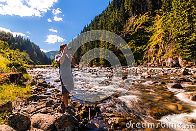 Hiker stops on the mountain river bank to take a picture Stock Photo