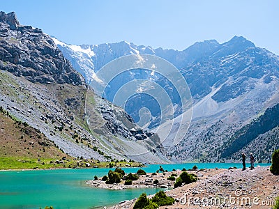 Hikers with backpack near Kulikalon lake on rocky mountain background. Fann Mountains, Tajikistan, Central Asia Stock Photo