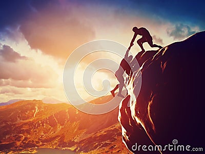 Hikers climbing on rock, giving hand and helping to climb Stock Photo