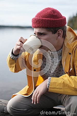 Hipster traveler in yellow raincoat holding metal mug. Stock Photo