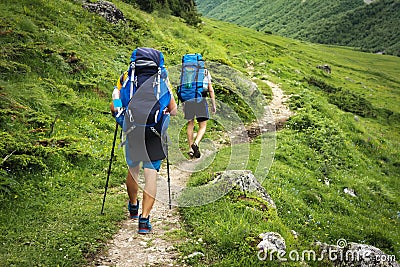 Hiking trail in Svaneti region, Georgia. Two hikers men walk on trek in mountain. Tourists with backpacks hike in highlands Stock Photo