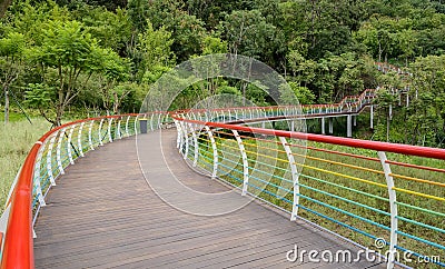 Hillside planked walkway with colorful steel railings in woods Stock Photo