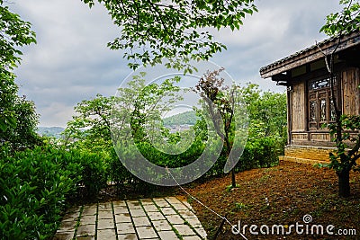 Hillside tile-roofed wooden building by path in cloudy spring af Stock Photo