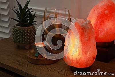 Himalayan salt lamps, candles, houseplant and gemstones on wooden table near white wall indoors Stock Photo
