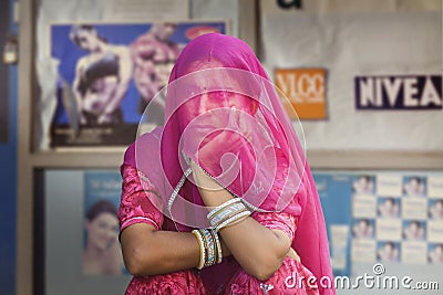 Hindu women covered by a violet scarf from a conservative fam in front of a billboard full of pictures of women in modern clothing Editorial Stock Photo