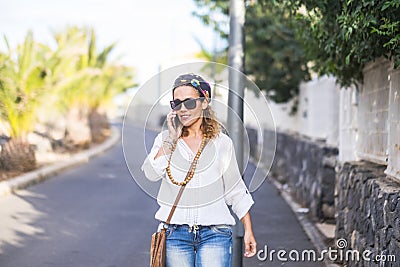 Hippy people portrait with attractive blonde middle age woman walking and calling at the phone on the street in outdoor leisure Stock Photo