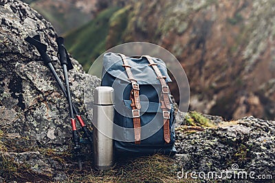 Hipster Blue Backpack, Thermos And Trekking Poles Closeup, Front View. Tourist Traveler Bag On Rocks Background. Adventure Hiking Stock Photo