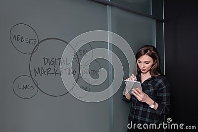 Hipster freelancer woman holding a tablet and standing near a business idea sketch on blackboard Stock Photo