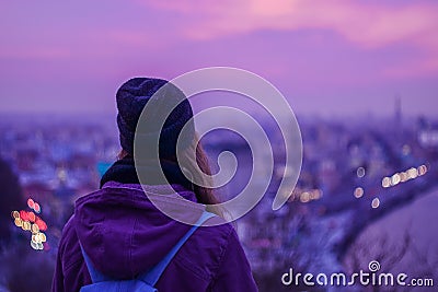 Hipster girl traveler looking at winter evening cityscape, purple violet sky and city lights Stock Photo