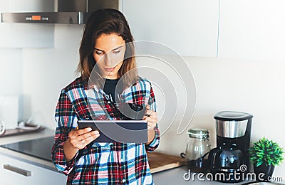 Hipster girl using tablet technology and drink coffee in kitchen, girl person holding computer on background interior cuisine, fem Stock Photo