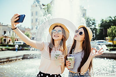 Hipster young girls in sunglasses best friends drink cocktails doing self photo and laughing in city street Stock Photo