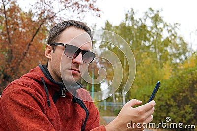 Hipster guy using smartphone device outdoor, outdoor portrait of young cheerful man texting an sms message at social networks, tec Stock Photo