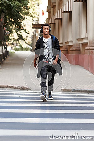 Hipster guy walking with atitudine on the crosswalk listening a music, goes to work in day time, promotes walking. Stock Photo
