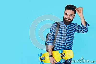 Hipster man over colorful blue background holding yellow skateboard Stock Photo