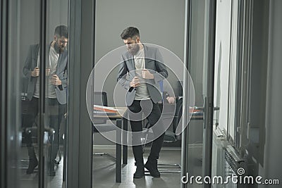 Hipster in modern office with glass walls. Bearded man seen in room door. Confident businessman in casual suit at Stock Photo