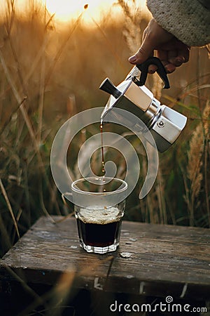 Hipster pouring fresh hot coffee from geyser coffee maker into glass cup in sunny warm light in rural countryside herbs. Stock Photo
