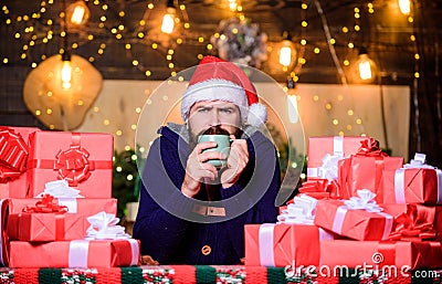 Hipster prepared gifts for family. Happy winter holidays. Warming up. Tea time. Man bearded santa claus hat drinking hot Stock Photo