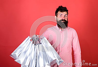 Hipster on smiling face is shopping addicted or shopaholic. Guy shopping on sales season with discounts. Man with beard Stock Photo