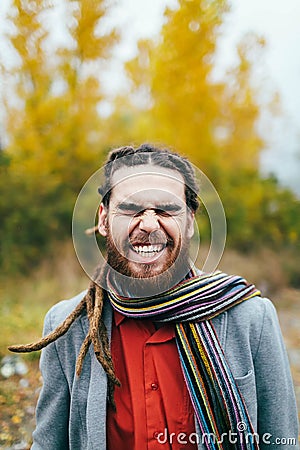 Hipster is smiling. A stylish man with dreadlocks and beard in a red shirt and grey jacket. Groom posing on nature Stock Photo