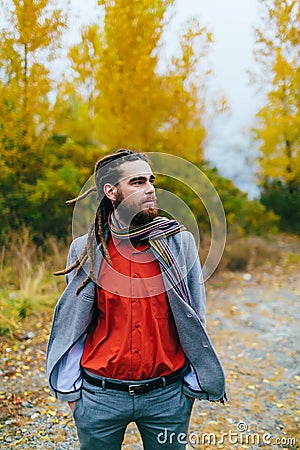 Hipster. A stylish man with dreadlocks and beard in a red shirt and grey jacket. Groom posing on nature. Autumn wedding Stock Photo