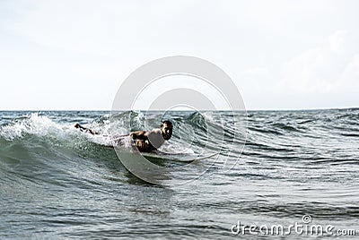 Hipster surfer slipping on the waves lying on his board with a big wave in sea - Bearded man training with surfboard to sea - Stock Photo