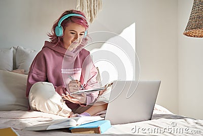 Hipster teen girl student with pink hair watch online webinar learning in bed. Stock Photo