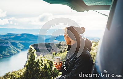 Hipster tourist hold in hands mug of hot drink, lonely smile guy enjoy sun flare mountain in auto, traveler drink cup of tea Stock Photo