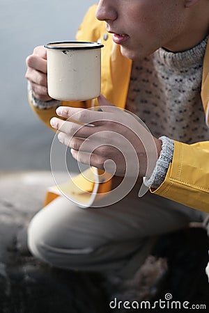 Hipster traveler in yellow raincoat holding metal mug. Stock Photo