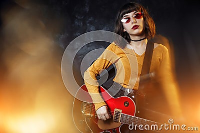 Hipster woman with curly hair play red guitar in neon lights. Rock musician is playing electrical guitar. Stock Photo