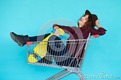 Hipster woman with yellow skateboard sitting in shopping trolley Stock Photo