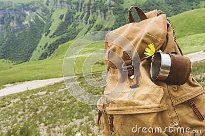 Hipster yellow vintage backpack with a mug fixed on it with a mug close-up front view. Traveler`s travel bag in the Stock Photo