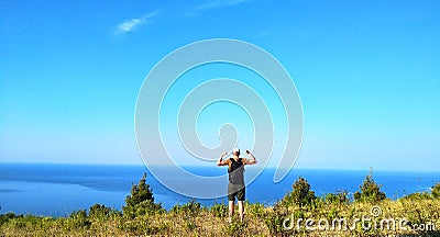 Hipster young man with backpack enjoying sunrise on peak of mountain. Male tourist traveler shows biceps after climbing mountain Stock Photo