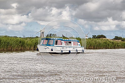 Hired boat sales pass windmills on Norfolk Broads Editorial Stock Photo