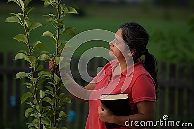 Hispanic Christian Woman Contemplating her Pear Tree After Working Her Yard and Having Meditation Stock Photo