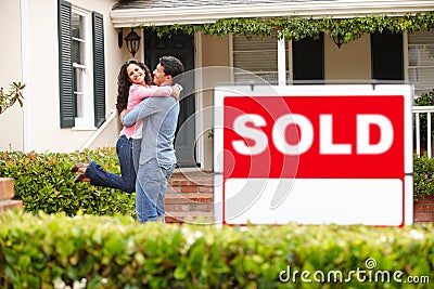 Hispanic couple outside home with sold sign Stock Photo