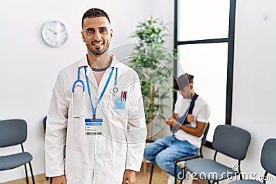 Hispanic doctor man at waiting room with pacient with arm injury looking positive and happy standing and smiling with a confident Stock Photo