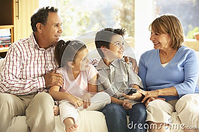 Hispanic Grandparents With Grandchildren Relaxing On Sofa At Home Stock Photo