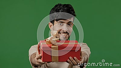 Hispanic happy man giving gift large red box with gold ribbon studio green background portrait friendly indian guy Stock Photo