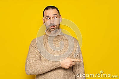 Hispanic man with a beard in a beige turtleneck pointing to the side with his index finger while looking sideways Stock Photo