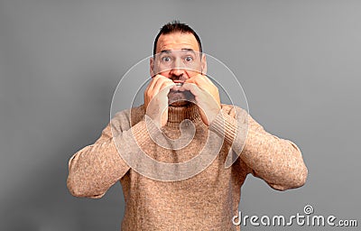 Hispanic man in his 40s scared and shocked biting his nails, staring wide-eyed at something horrible, wearing a Stock Photo