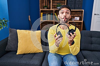 Hispanic man holding broken headphones making fish face with mouth and squinting eyes, crazy and comical Stock Photo